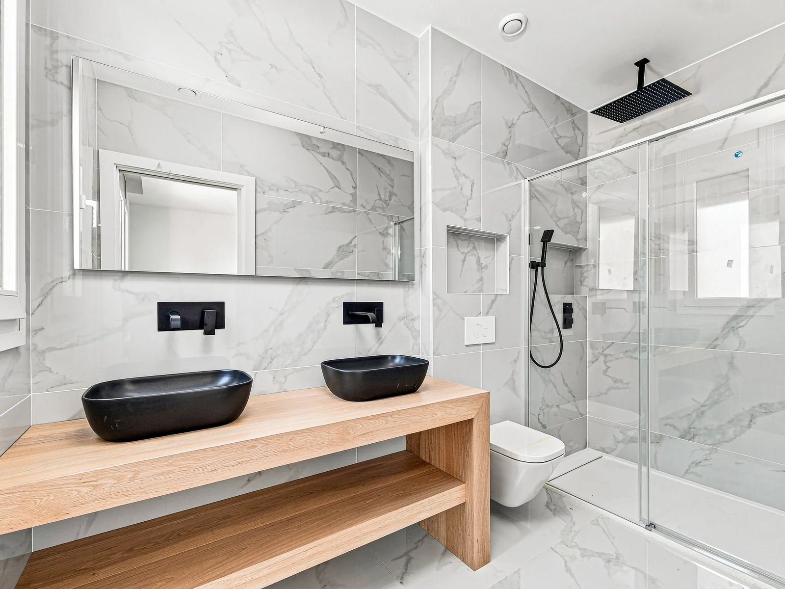 Baño de mármol con encimera de madera maciza y lavabos negros, villa en Castelldefels