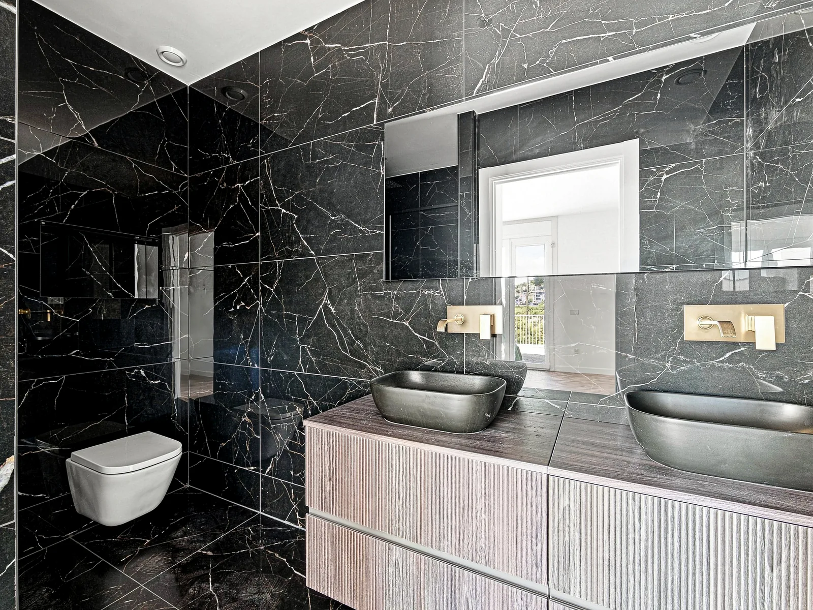 Baño de mármol negro con mueble ranurado y grifería dorada, villa en Castelldefels