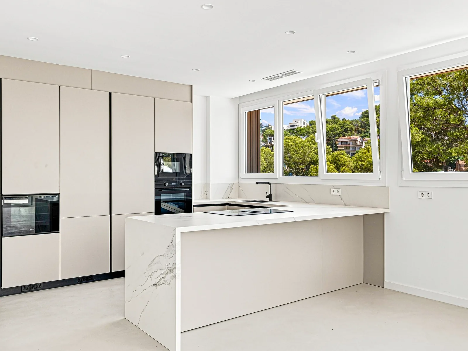 Cocina con isla de mármol y columna de hornos, villa en Castelldefels